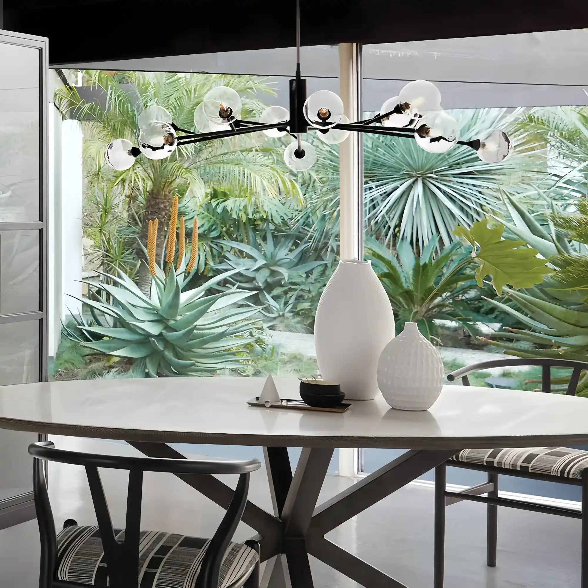 Modern dining room with a chandelier, table, and chairs in front of a large window with greenery outside.