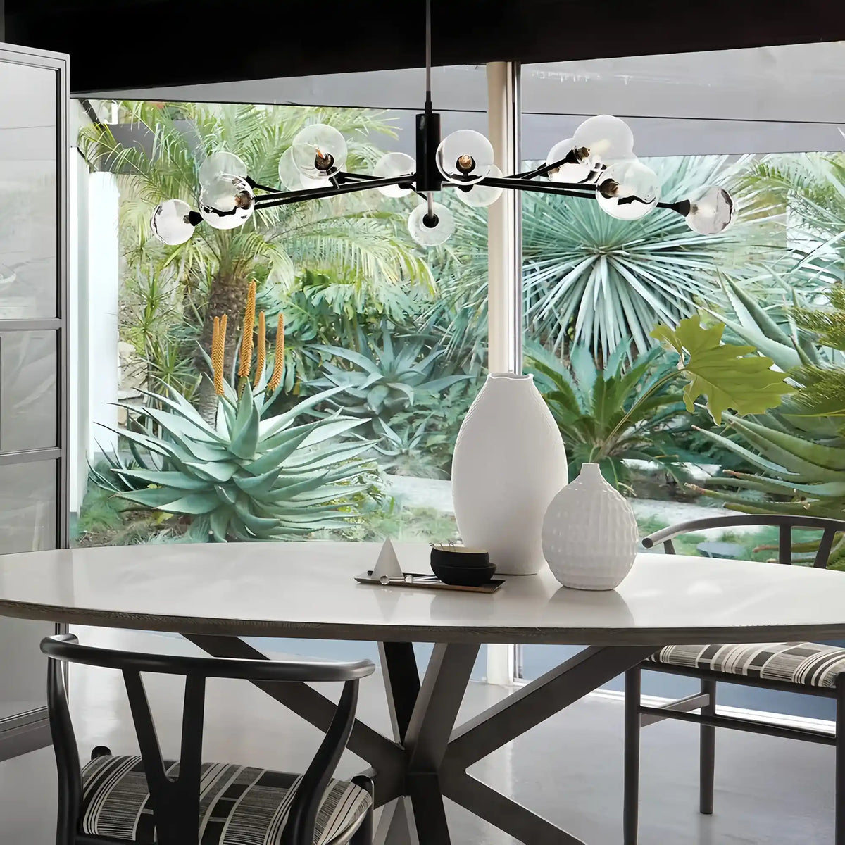 Modern dining room with a chandelier, table, and chairs in front of a large window with greenery outside.
